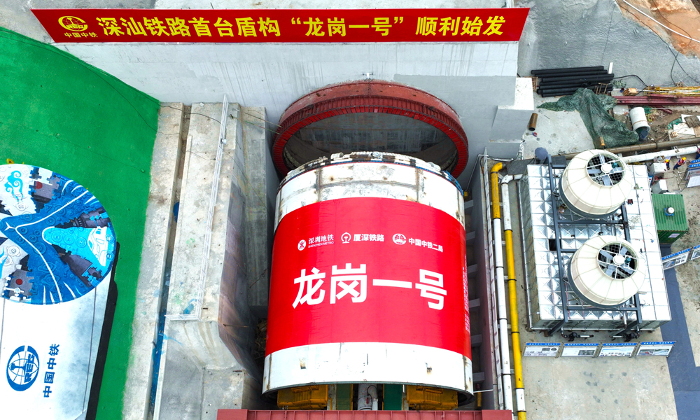 深汕鐵路是“八縱八橫”高鐵主通道中沿海高速通道的重要組成部分，起于深圳樞紐西麗站，終至深汕合作區并引入廣汕鐵路深汕站，正線全長125.52公里。由中鐵二局組織施工的深汕鐵路龍崗隧道盾構掘進全段并行廈深高鐵，先后穿越21處重要建構筑物，長距離穿越巖溶及軟硬不均與軟硬交互不良地質，是深汕鐵路重點控制性工程之一。龍崗隧道進口段分為南約和寶荷隧道兩個區間，“龍崗一號”盾構機負責南約盾構區間的掘進任務。圖為“龍崗一號”盾構機始發現場。