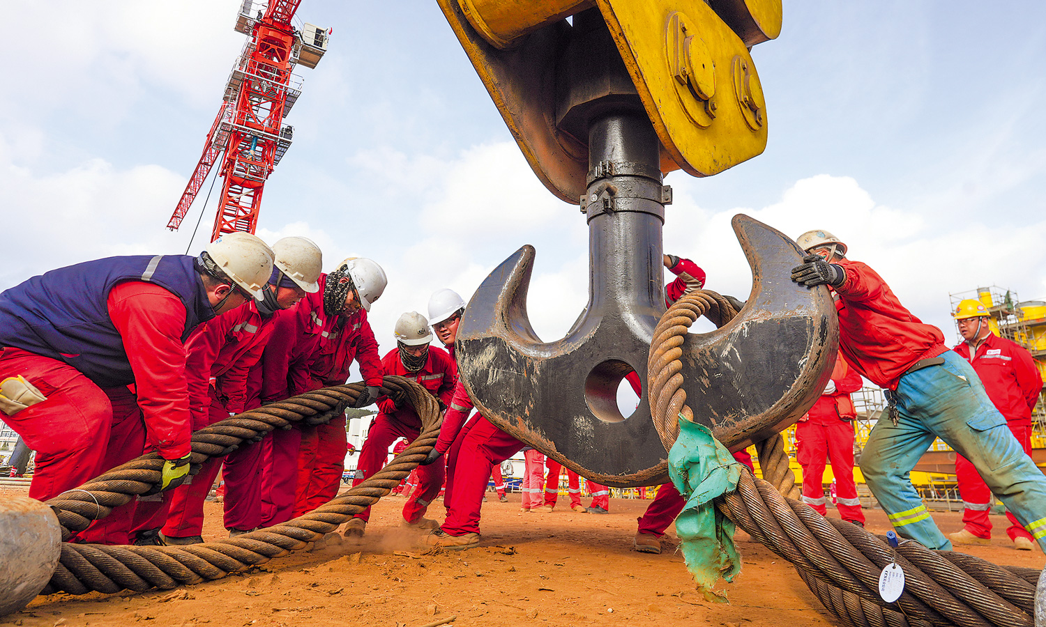 在中國海油海油工程制造場地，施工人員合力將大直徑鋼絲繩掛扣在吊鉤上。