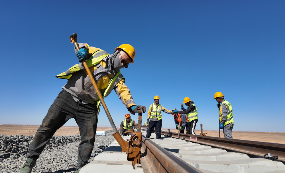 項目通車后將完善阿爾及利亞國家鐵路網，助力該國南部省份互聯互通，助力當地礦業發展。圖為中阿建設者進行鋪軌作業。