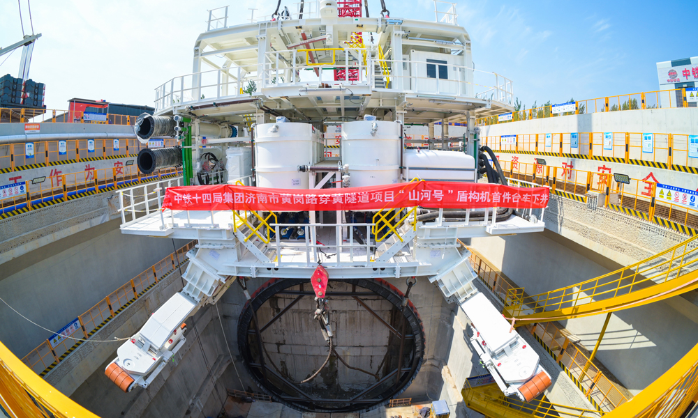 針對項目地質情況量身定制的“山河號”，最大開挖直徑17.5米，盾構機總長163米、重達5200噸、裝機總功率12580千瓦，盾構機總裝達到世界先進水平。本次吊裝下井的一號臺車，是“山河號”盾構機后配套臺車中最大、最關鍵的一節，重510噸，長約30米；設計為三層框架結構，搭載盾構機掘進的主要設備?？紤]其龐大的尺寸和重量，分三段采用后、中、前的順序，由800噸履帶吊從始發井端頭依次吊裝下井，在井下指定位置完成組裝工作。圖為盾構機臺車下井。