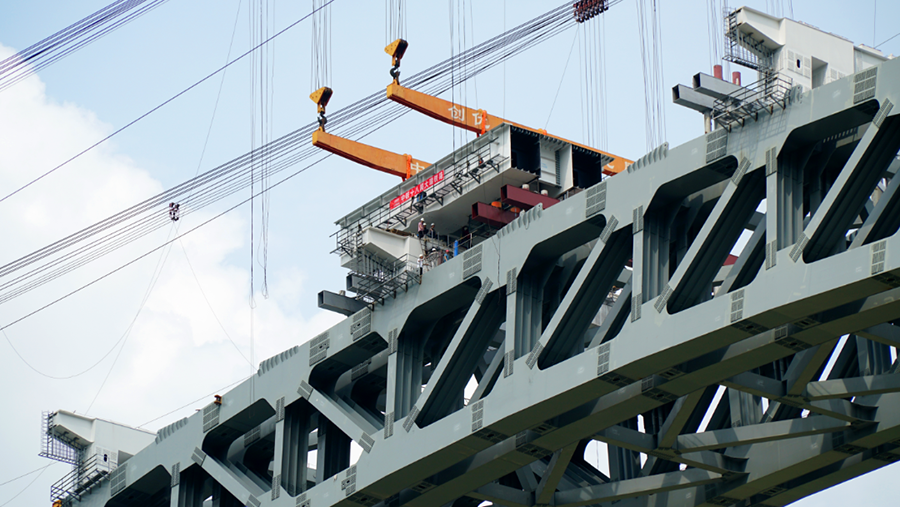 兩側引橋鋼混結合梁采用“步履式頂推”新工藝，均由大橋兩端向跨中方向頂推，在兩側分別搭設鋼混結合梁頂推平臺，并完成鋼混結合梁的拼裝、焊接、高強螺栓施擰及補涂裝等施工任務。圖為鋼箱梁節段落梁。