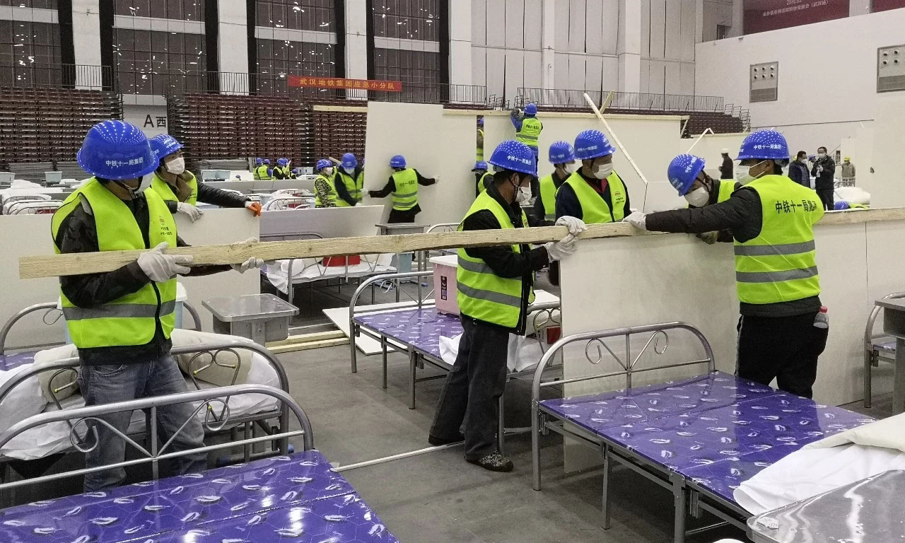 整個武漢客廳“方艙醫(yī)院”計劃在A、B、C三個廳布置2000個床位。此次增援主要負責武漢客廳“方艙醫(yī)院”A區(qū)12個倉位380多個病床隔板安裝、臨電安裝和門洞、吊頂、大門等施工任務(wù)。要求在最短時間內(nèi)完成施工任務(wù)，為早日收治新冠肺炎病人贏得時間。圖為隔板安裝現(xiàn)場。